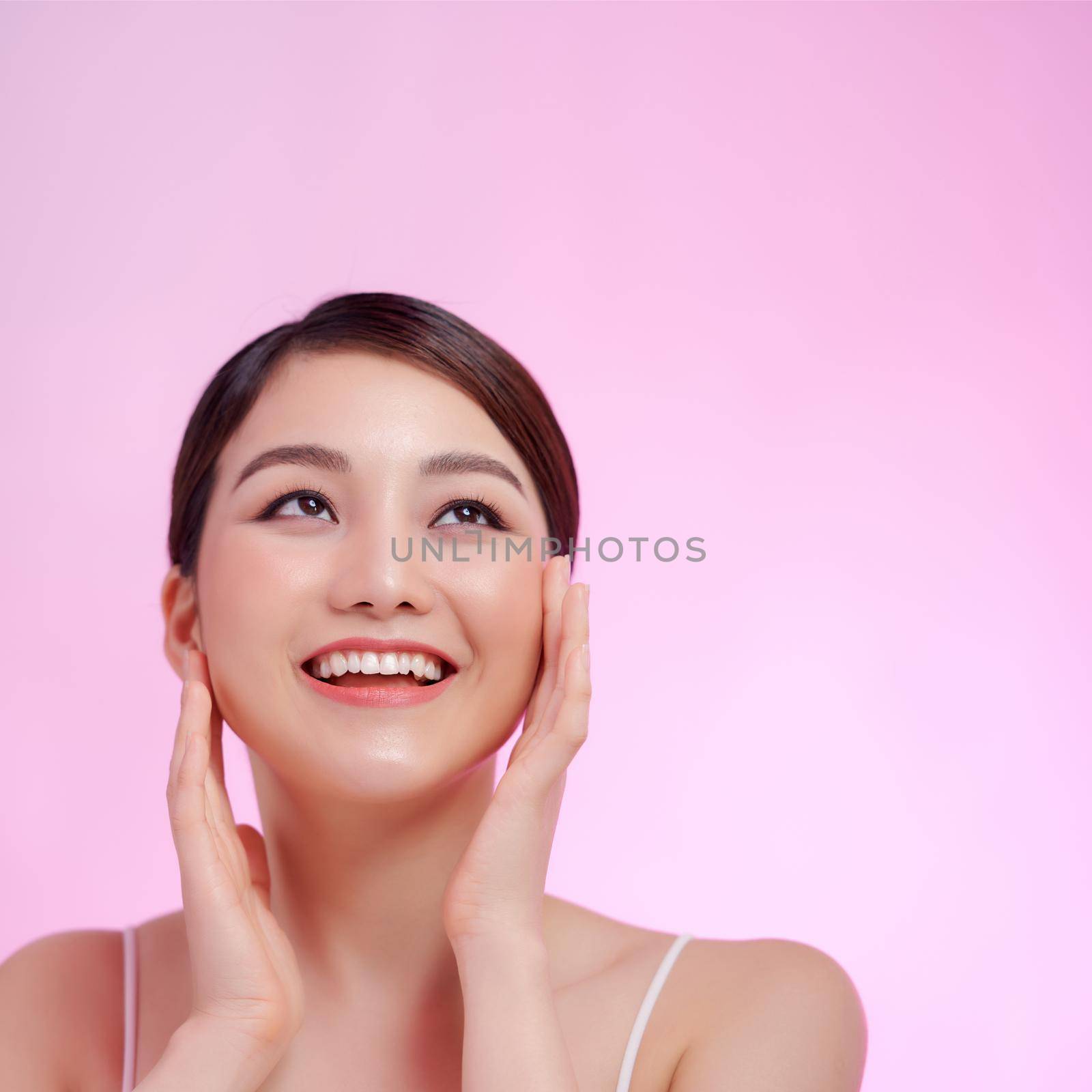 Woman close-up beauty portrait hands touching face on pink background by makidotvn