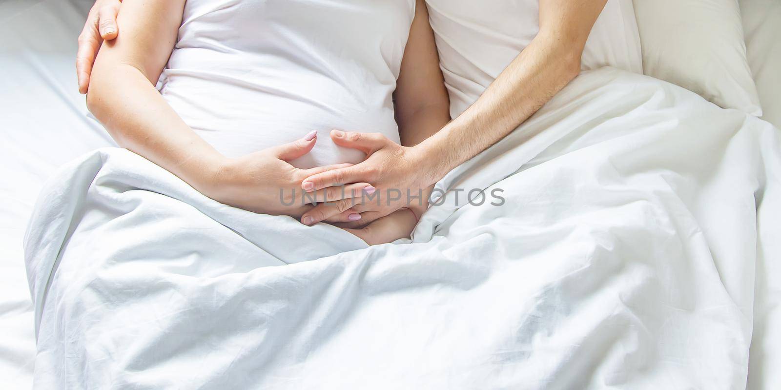 Pregnant woman with man hug belly in bed. Selective focus. by yanadjana