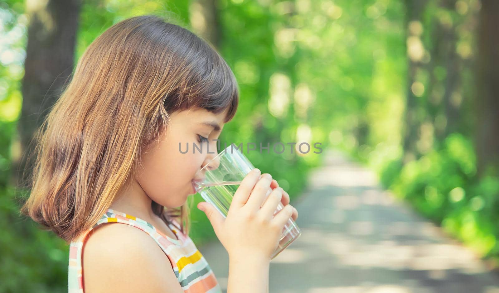 A child drinks water from a glass on the nature. Selective focus. Drink.