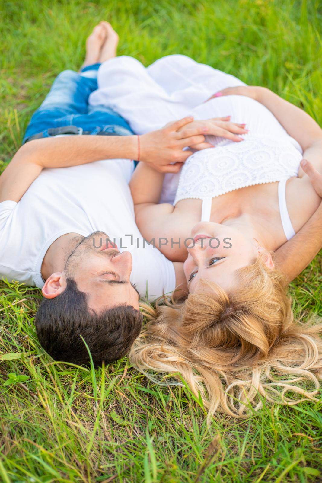 Pregnant woman and man photo shoot lie on the grass. Selective focus.