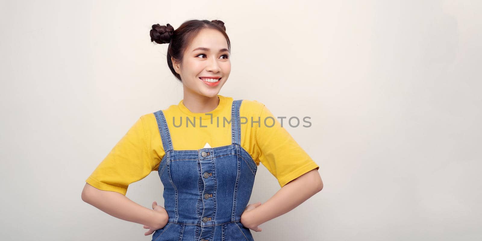 Beautiful young Asian woman is looking at camera and smiling, standing with akimbo studio shot isolated on white background by makidotvn
