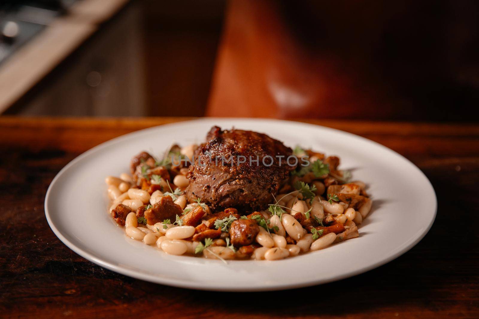 Professional chef cooking in kitchen. Tasty dish with beef steak and beans.