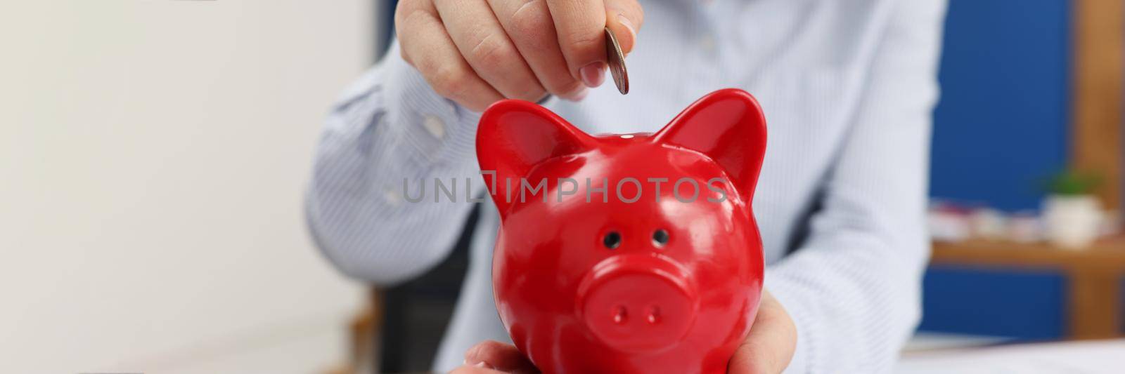 Business woman throwing coins into piggy bank at table with graphs closeup. Business investment concept