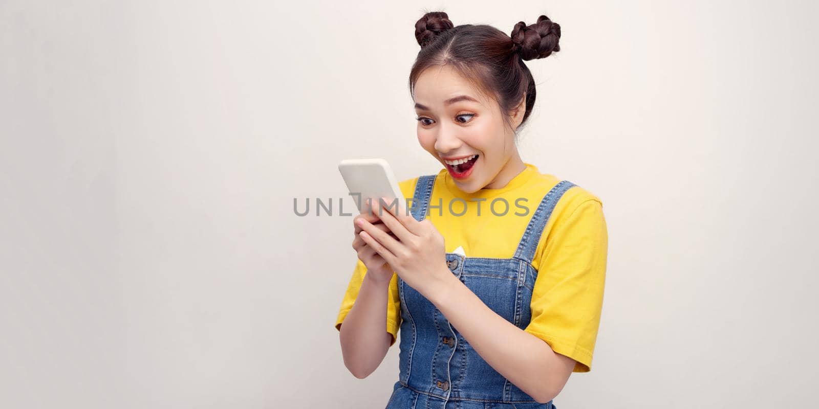 Portrait if a shocked young girl in dress looking at mobile phone isolated over white background by makidotvn