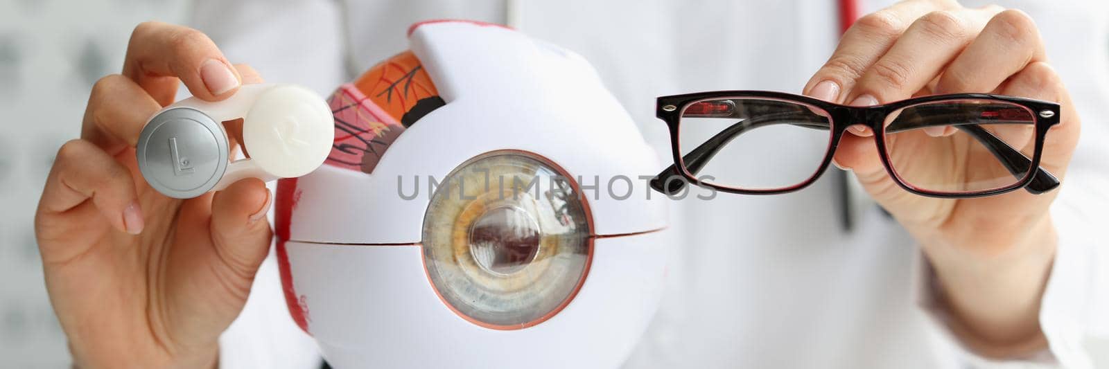 Ophthalmologist doctor holding eyeglasses and lenses near artificial model of eye closeup by kuprevich