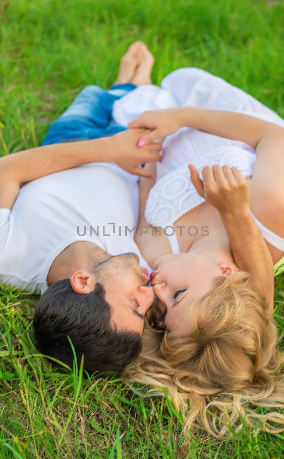 Pregnant woman and man photo shoot lie on the grass. Selective focus.