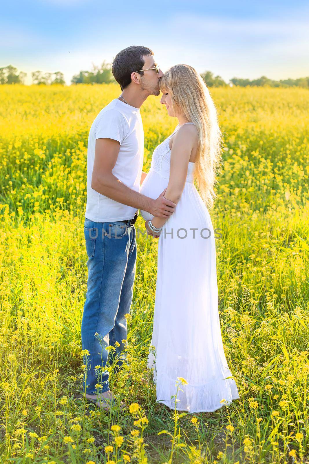 Pregnant woman and man photo shoot in mustard field. Selective focus.