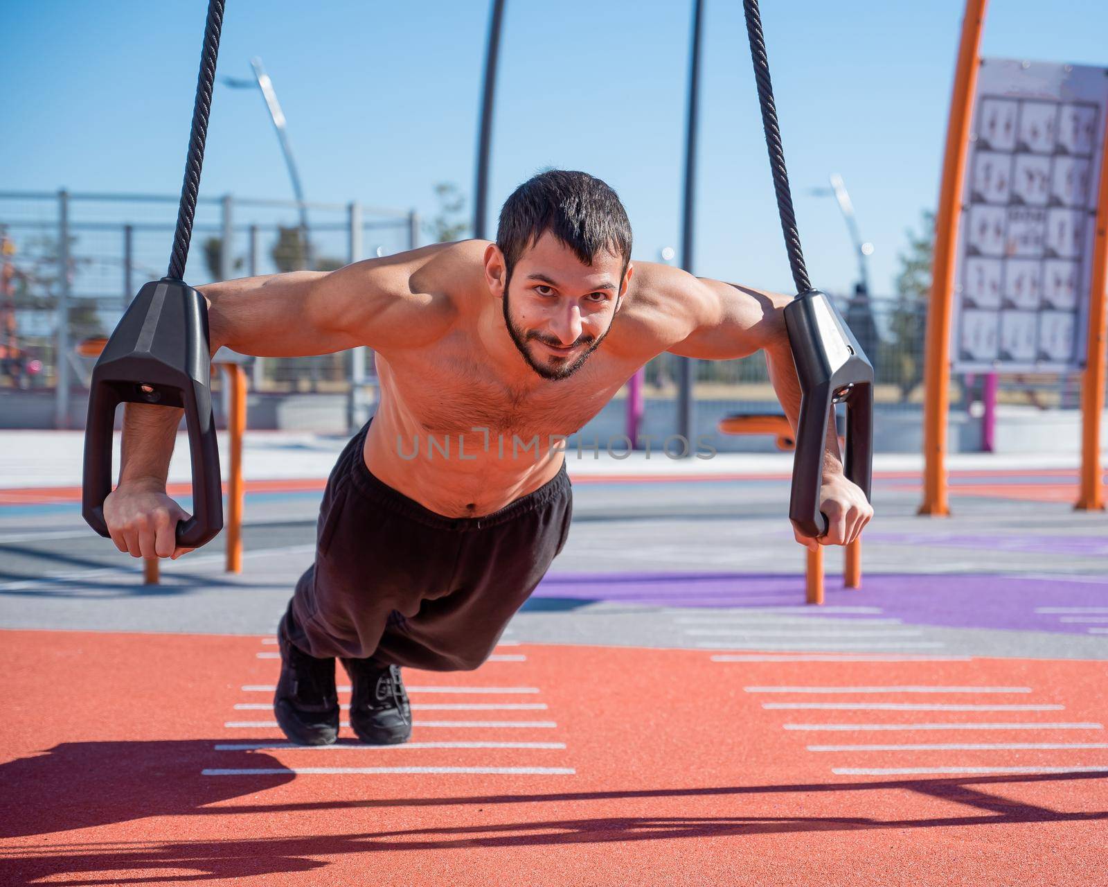 Shirtless man doing loop exercises outdoors