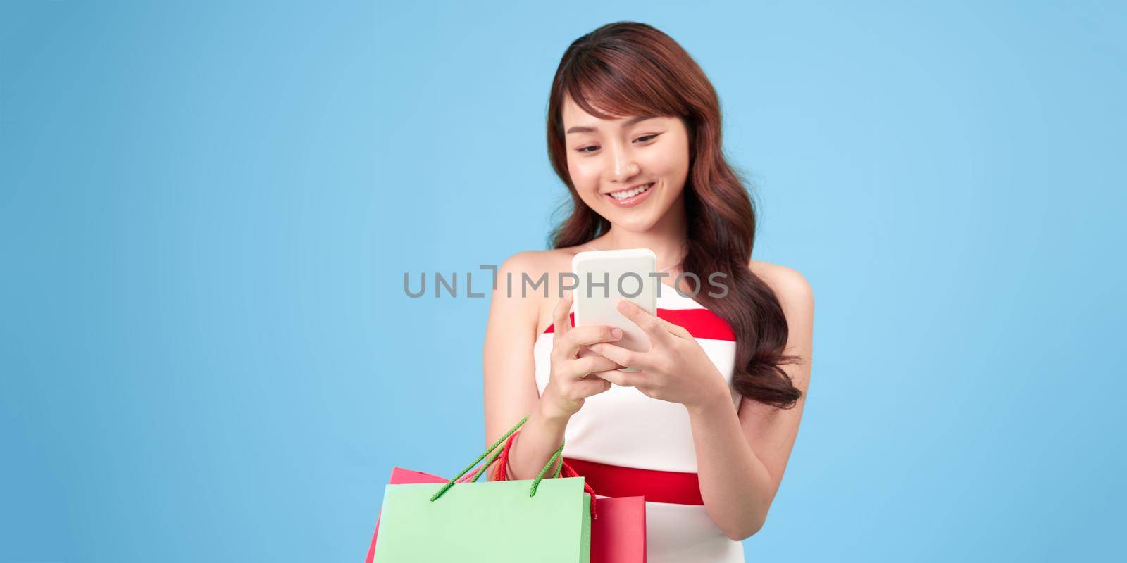 Happy beautiful asian woman carrying shopping bags on isolated blue background, summer sale concept. by makidotvn
