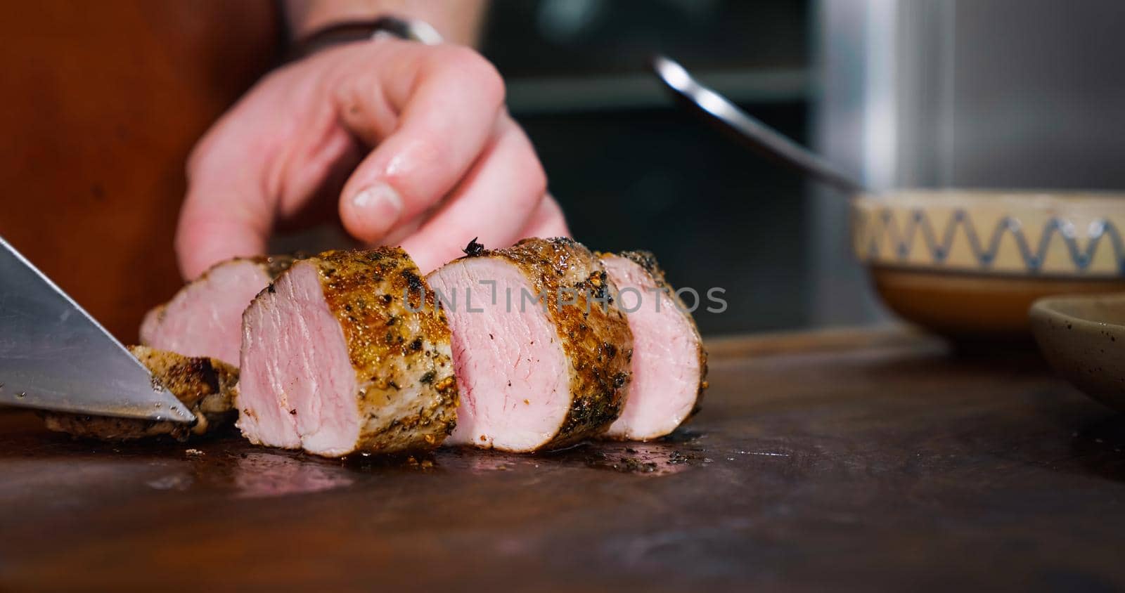 Chef Cuts Juicy Pork Steak on Rustic Cutting Board on Wooden Background. Concept of Delicious Meat Food. Close Up