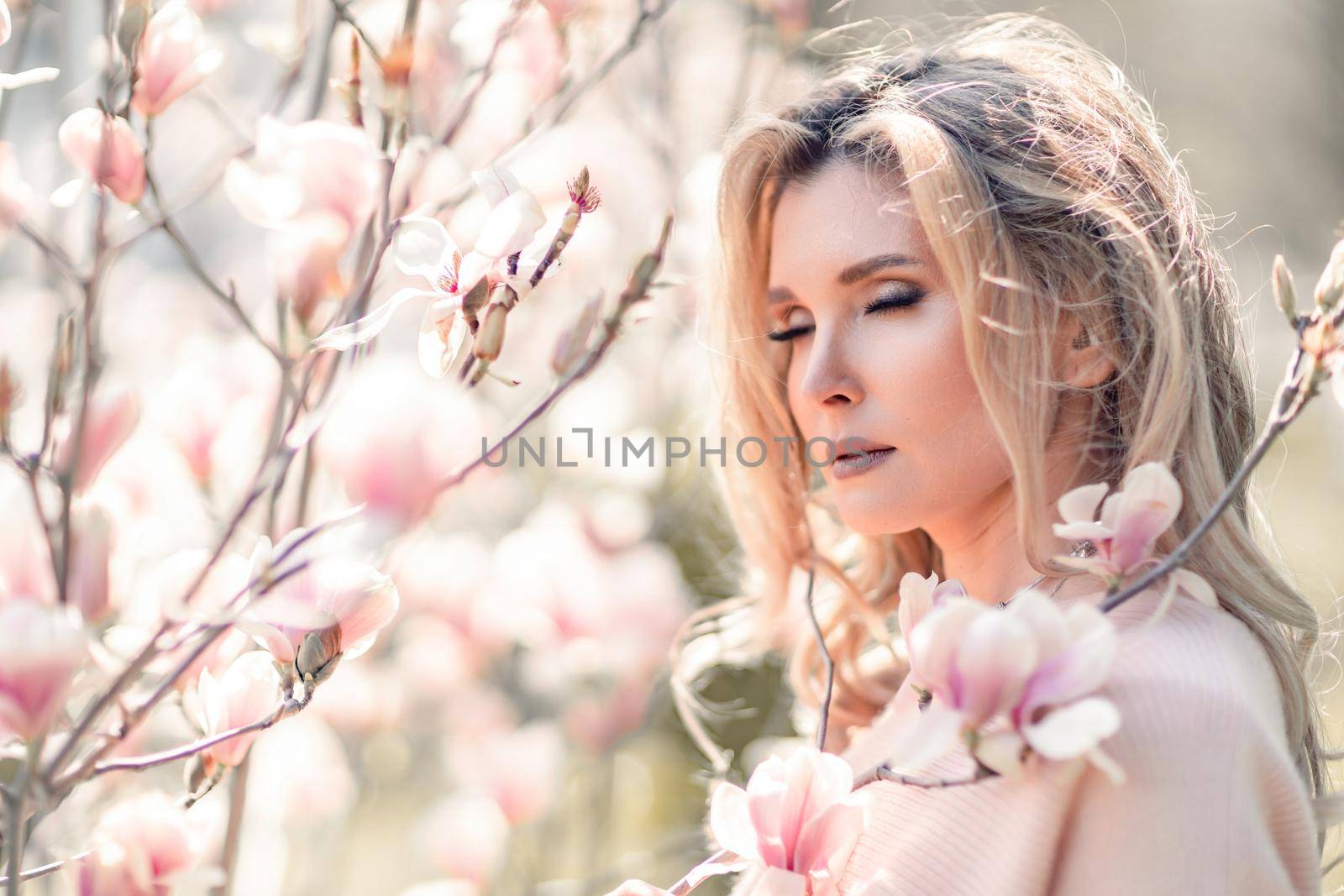 Portrait of a beautiful happy middle aged woman enjoying the smell in a blooming spring garden. Beautiful magnolia bushes, large flowers