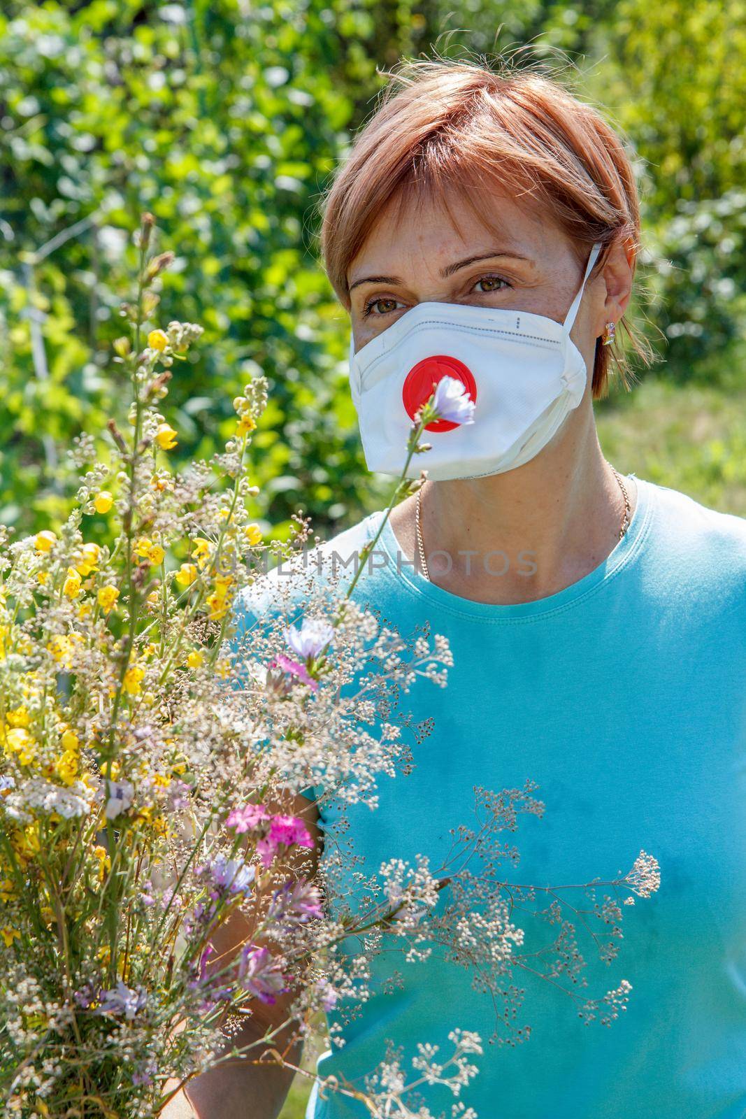 Woman in protective mask holding bouquet of summer wildflowers and trying to fight allergies to pollen. Allergy concept.