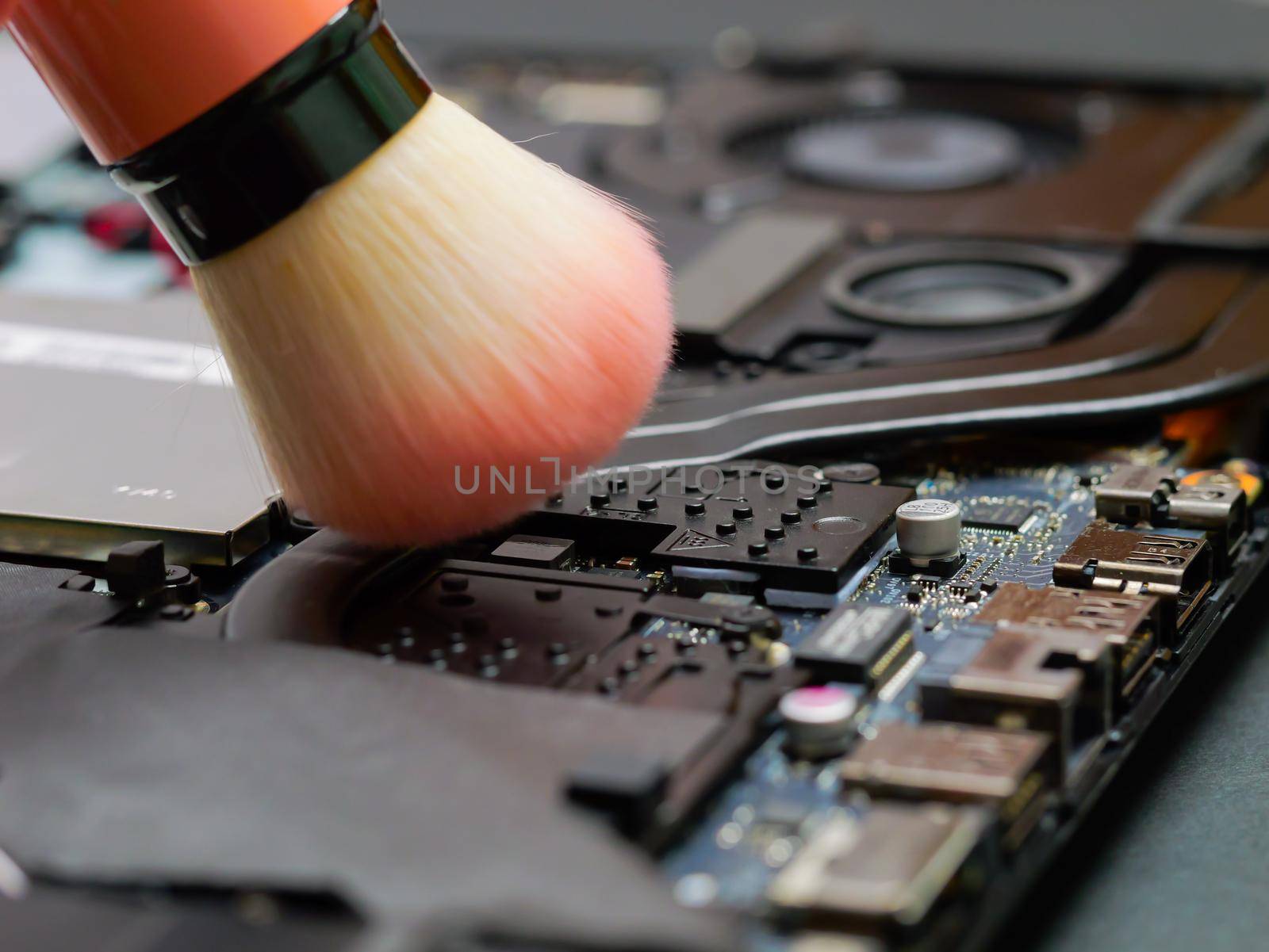 Close up man hands cleaning the cooler system of laptop during maintenance or prophylaxis, removing the dust with big brush. Repairs of electronic device concept. Indoors.