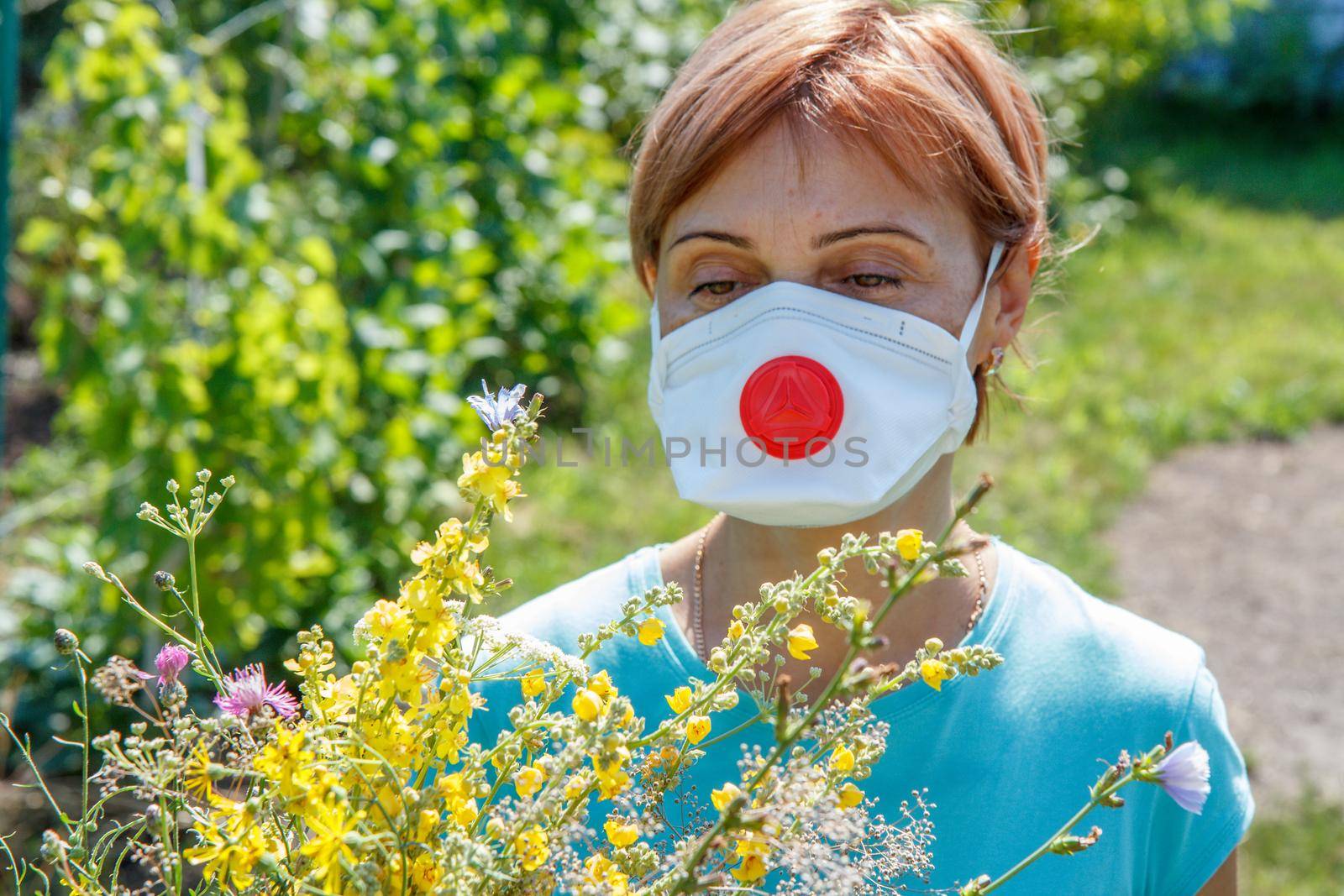 Woman in protective mask holding bouquet of wildflowers and trying to fight allergies to pollen. Natural daylight. Allergy concept.