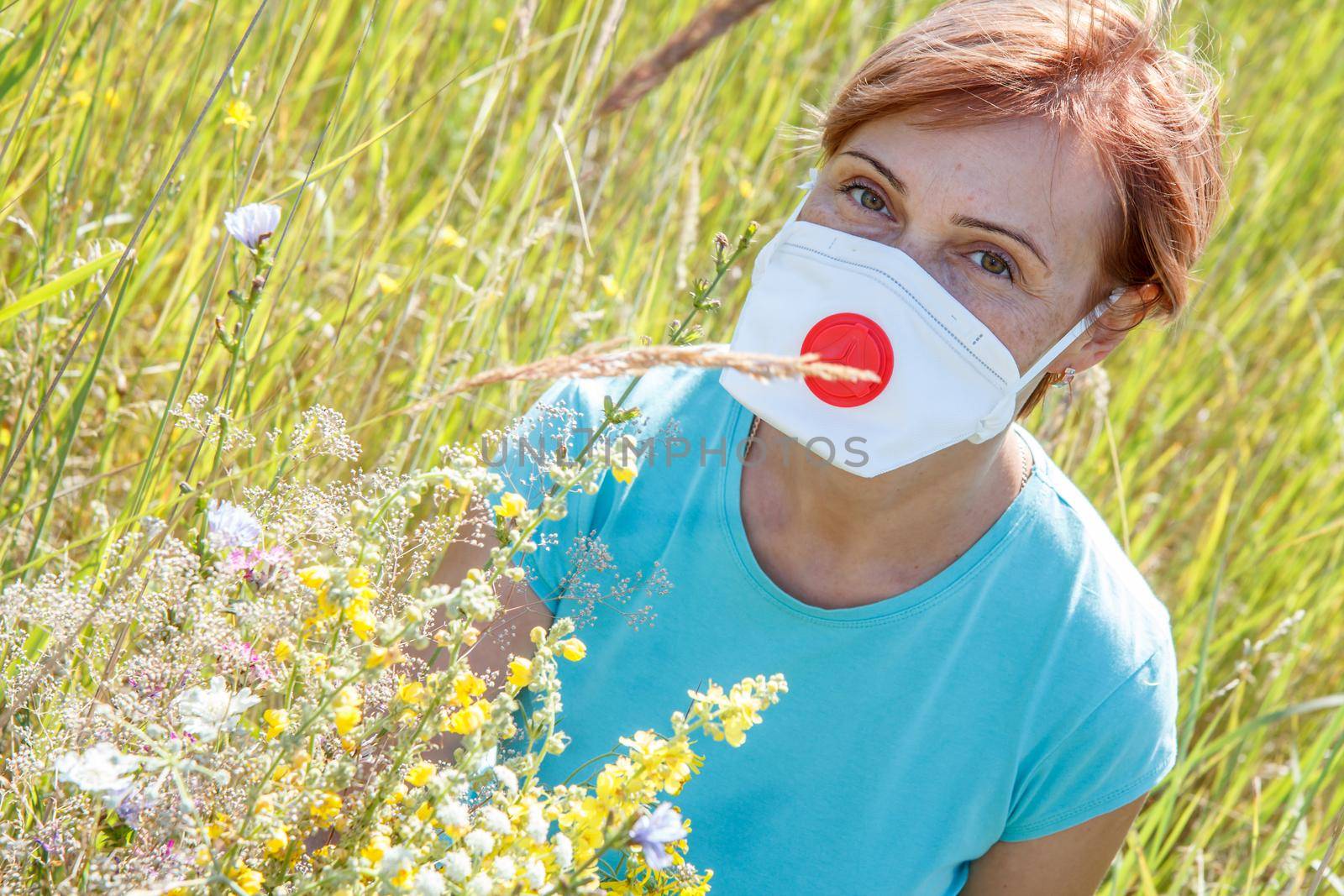 Woman in protective mask holding bouquet of wildflowers and trying to fight allergies to pollen. Natural daylight. Allergy concept.