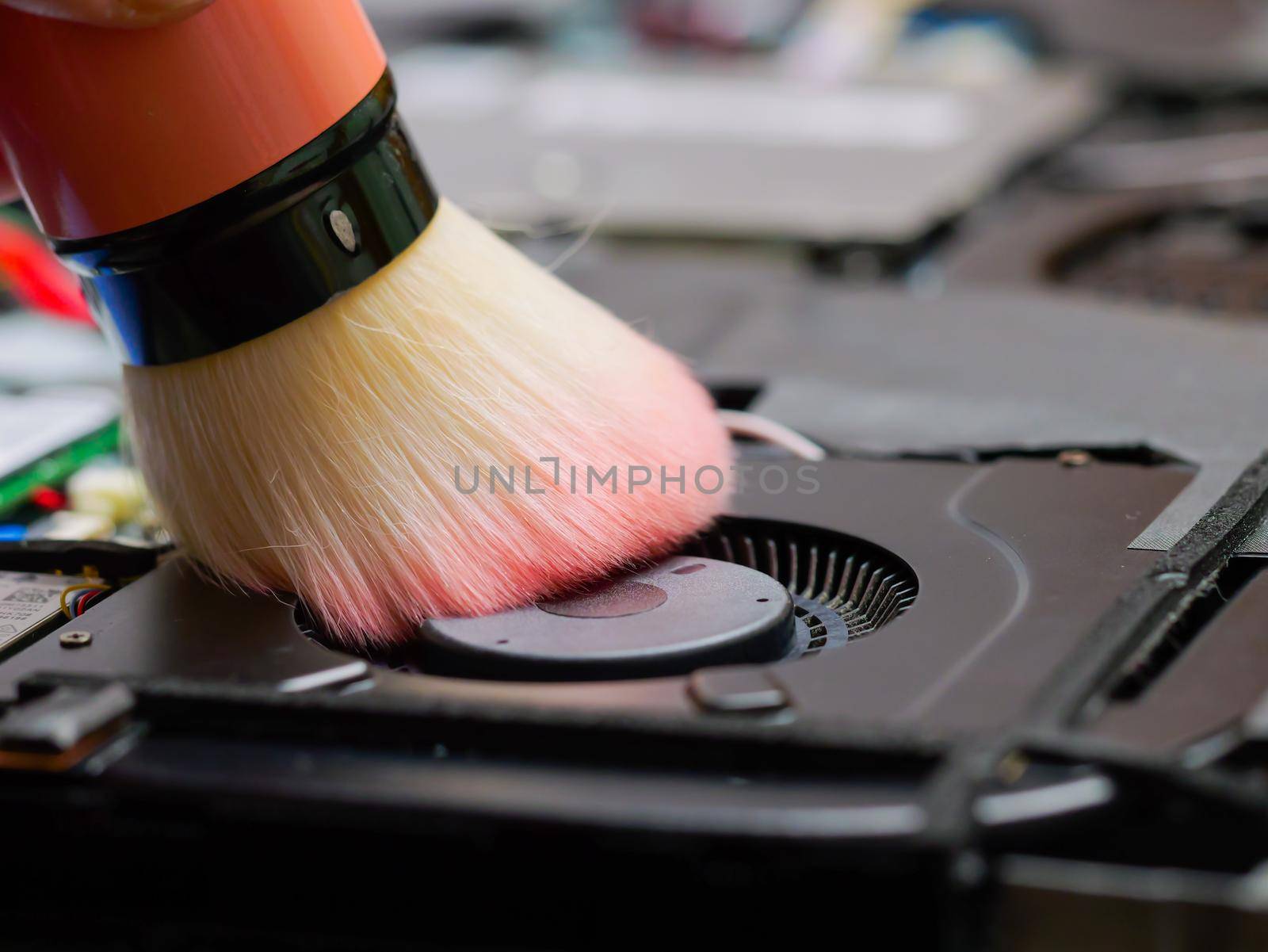 Macro of a brush cleaning a laptop fan at a professional service during maintenance or prophylaxis, removing the dust with brush. Repairs of electronic device concept. Indoors.