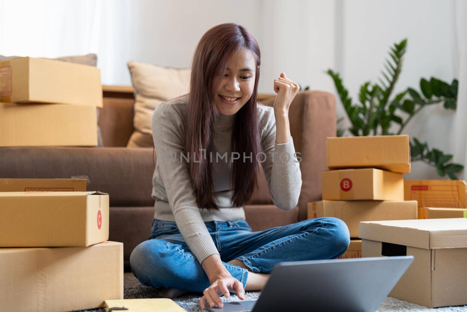 Asian woman working at small business ecommerce with laptop very happy and excited doing winner gesture with arms raised, smiling and screaming for success. celebration concept