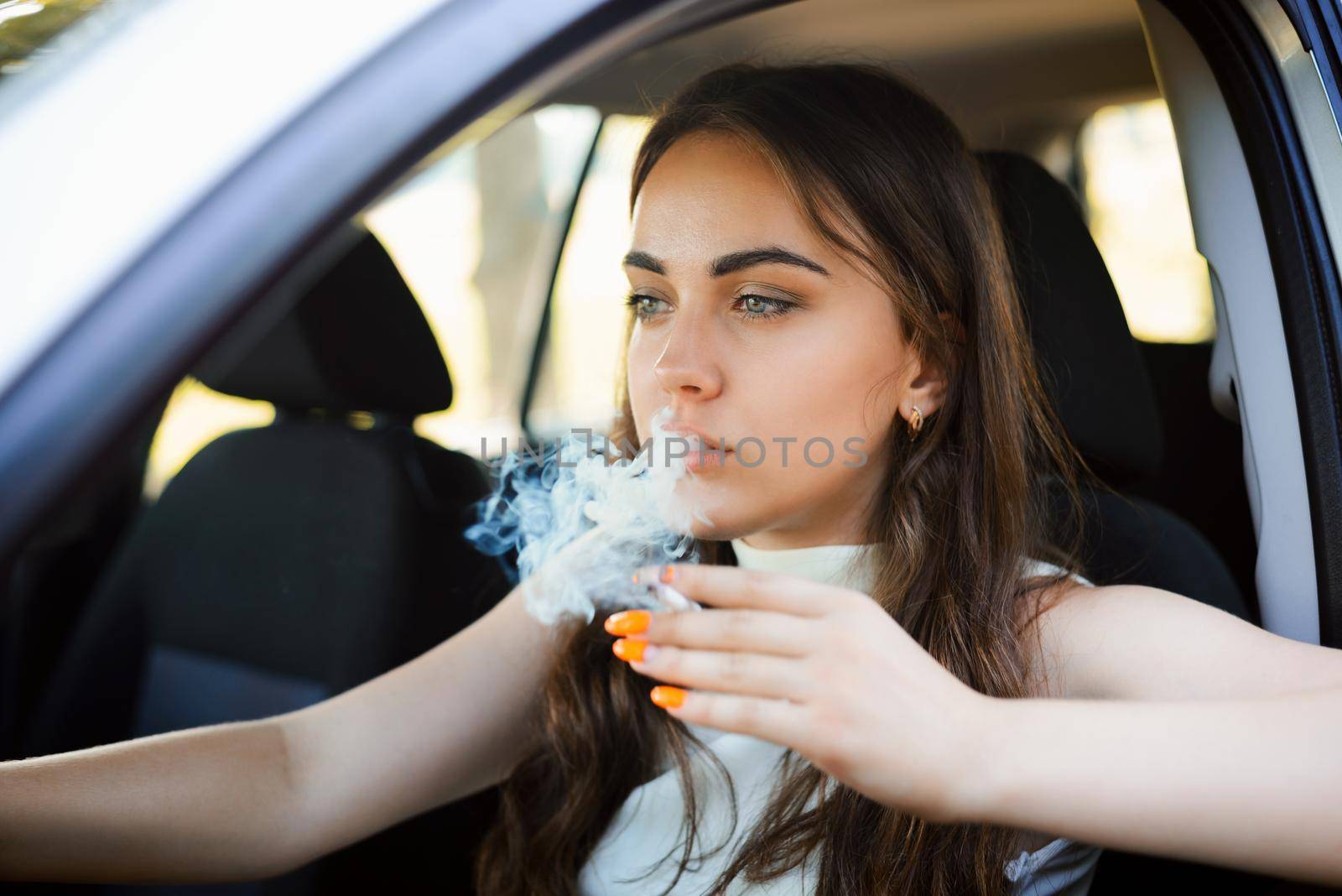 Young attractive girl smoking cigarette with a lot of smoke while driving a car