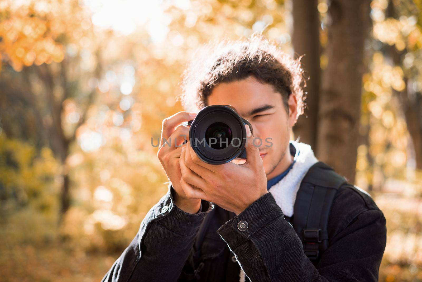 Male photographer with amateur camera taking picture of nature in the park in a sunny autumn day