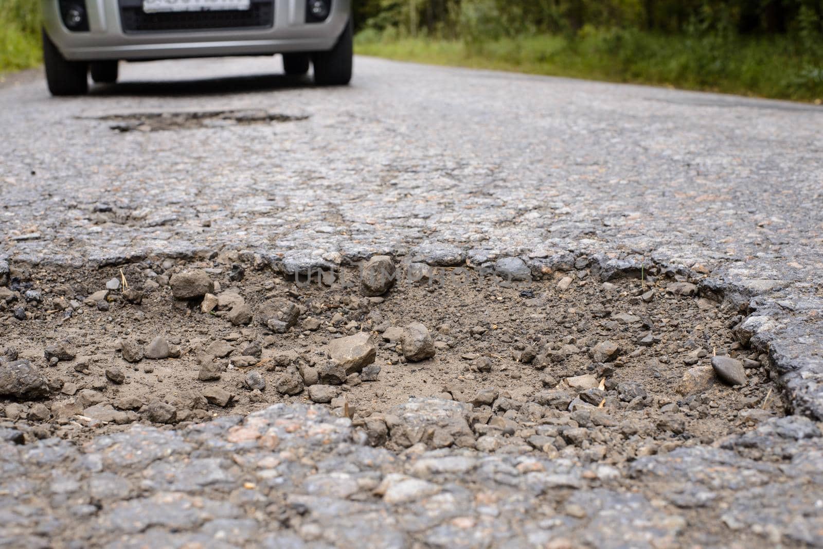 Pothole in asphalt road and car in the background by VitaliiPetrushenko