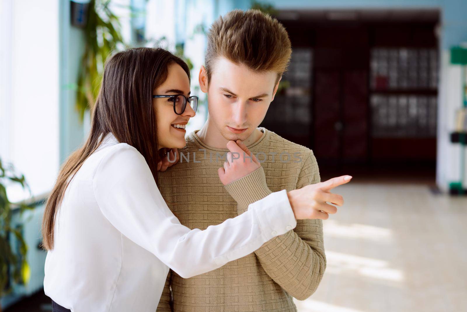 Female student gossiping about classmate to her friend and pointing someone, male friend listens attentively