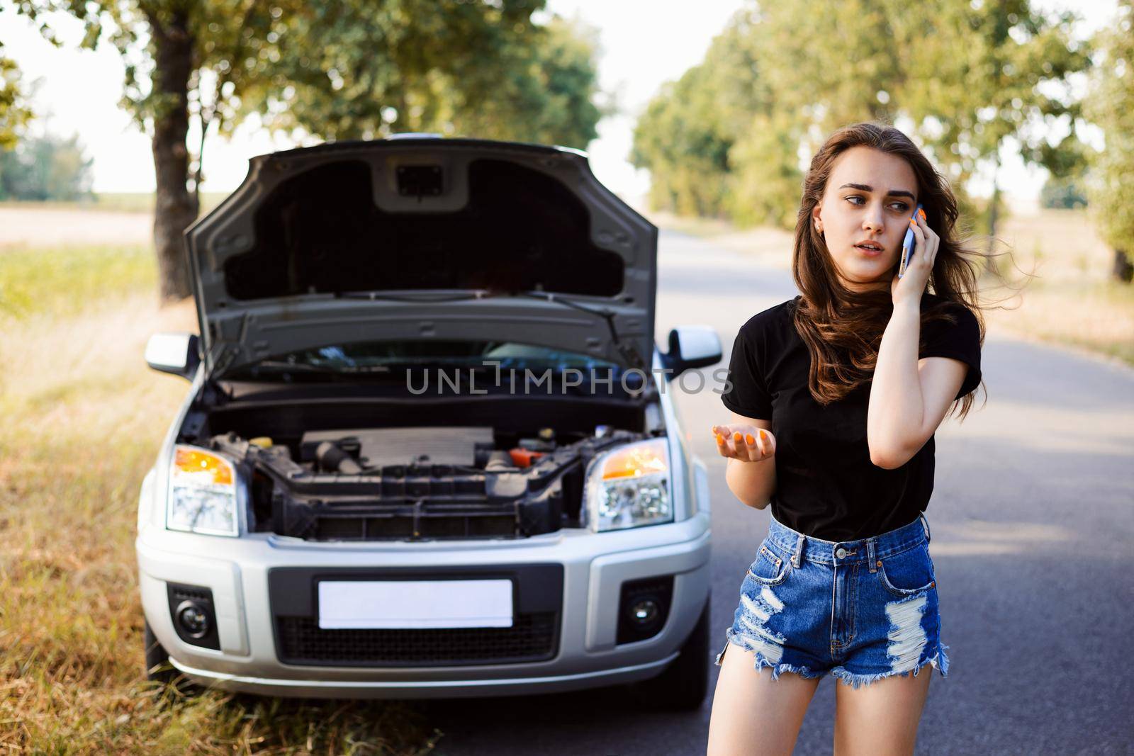 Car broke by the wayside of the asphalt road and young student driver calls the rescue team to help her and repair the car