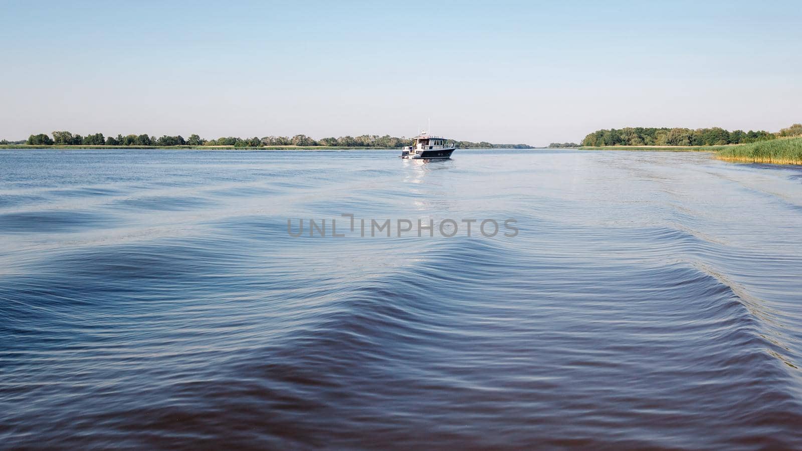 A large and wide rippling water and a small boat in the distance in the lagoon. by Lincikas