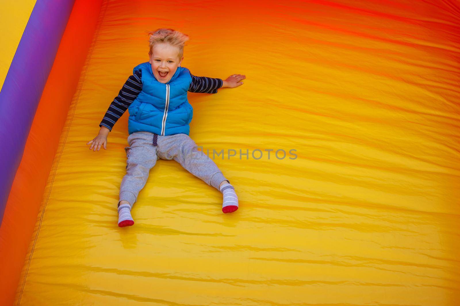Boy jumping down the slide on a yellow-orange inflatable bouncy castle. There is free space for text in the image.