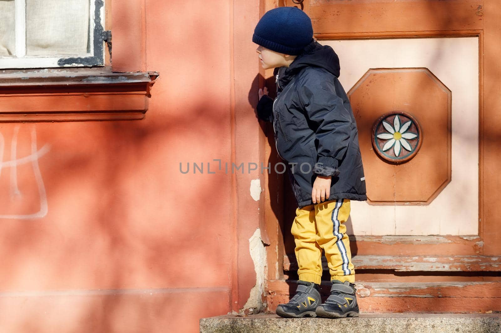 A cute little boy dressed in autumn is going for a walk in the old city with a hat by Lincikas