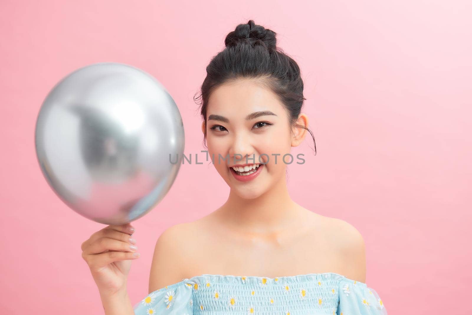 A woman holding silver balloon against a pink background