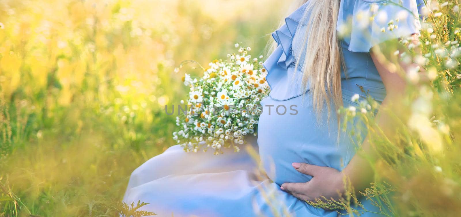 pregnant woman with camomiles in hands. Selective focus. by yanadjana