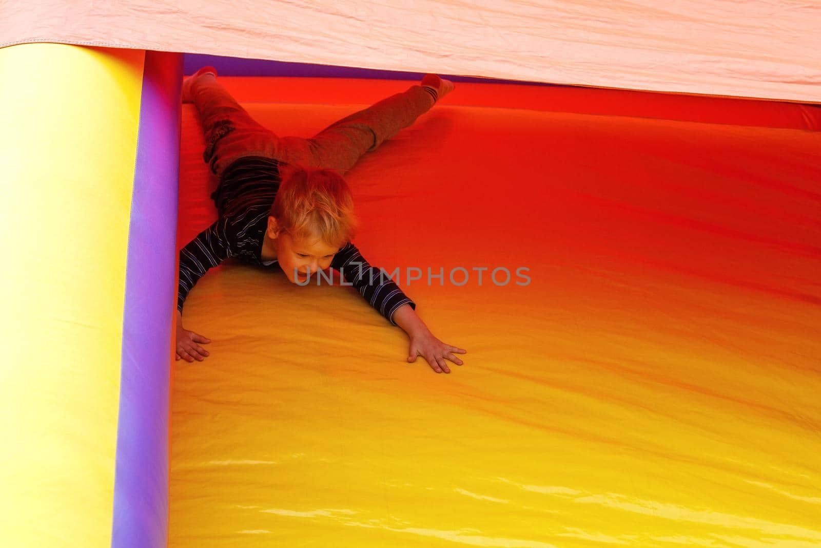 A cheerful boy slides his belly off a large, bright yellow trampoline at high speed.