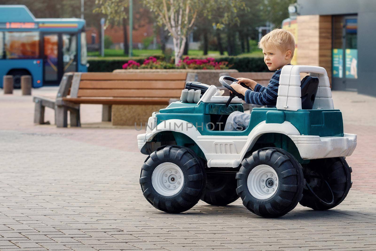 Little preschool kid boy driving big toy car and having fun outdoors. Child enjoying warm summer day in city landscape.