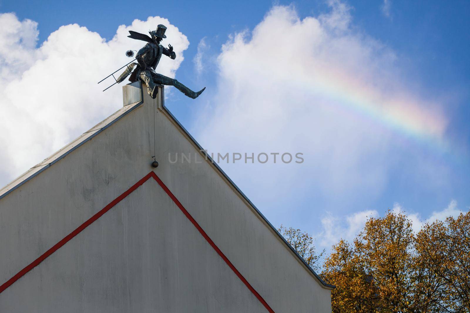 Chimney Sweeper Sculpture on roof in old town of Klaipeda, Lithuania. House wall in Klaipeda Old Town. Blue sky with white clouds and rainbow.