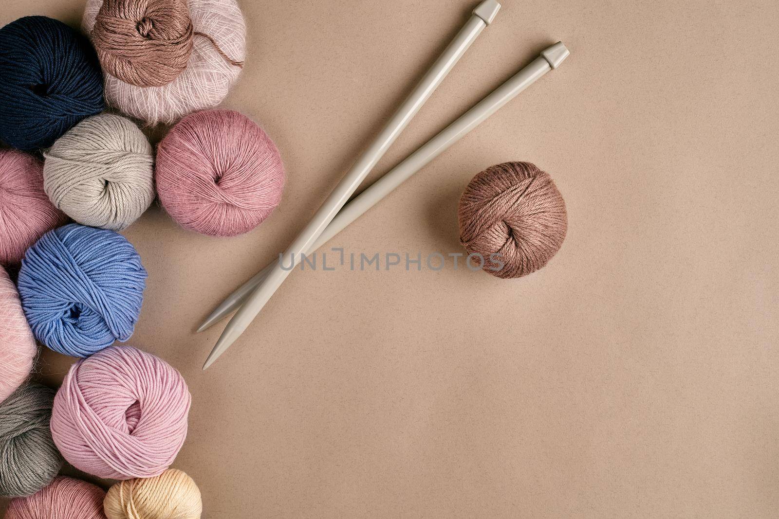 Set of colorful wool yarn on beige background. Knitting as a kind of needlework. Colorful balls of yarn and knitting needles. Top view. Still life. Copy space. Flat lay