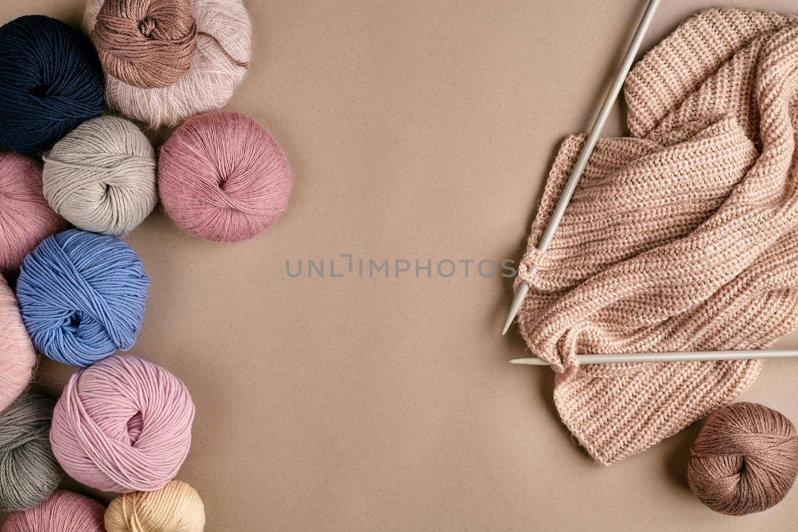 Set of colorful wool yarn and knitting on knitting needles on beige background. Knitting as a kind of needlework. Colorful balls of yarn and knitting needles. Top view. Still life. Copy space. Flat lay