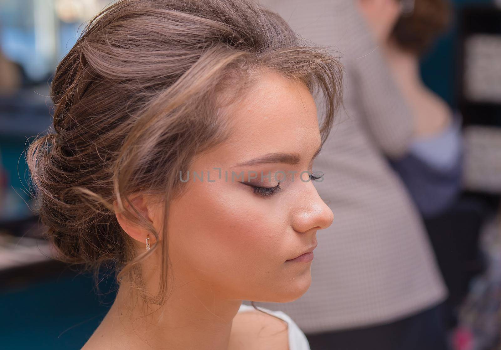 Girl's face with closed eyes, fashionable make-up and hairstyle. Female master makes makeup to a young woman. Business concept - beauty salon, facial skin care, cosmetology.