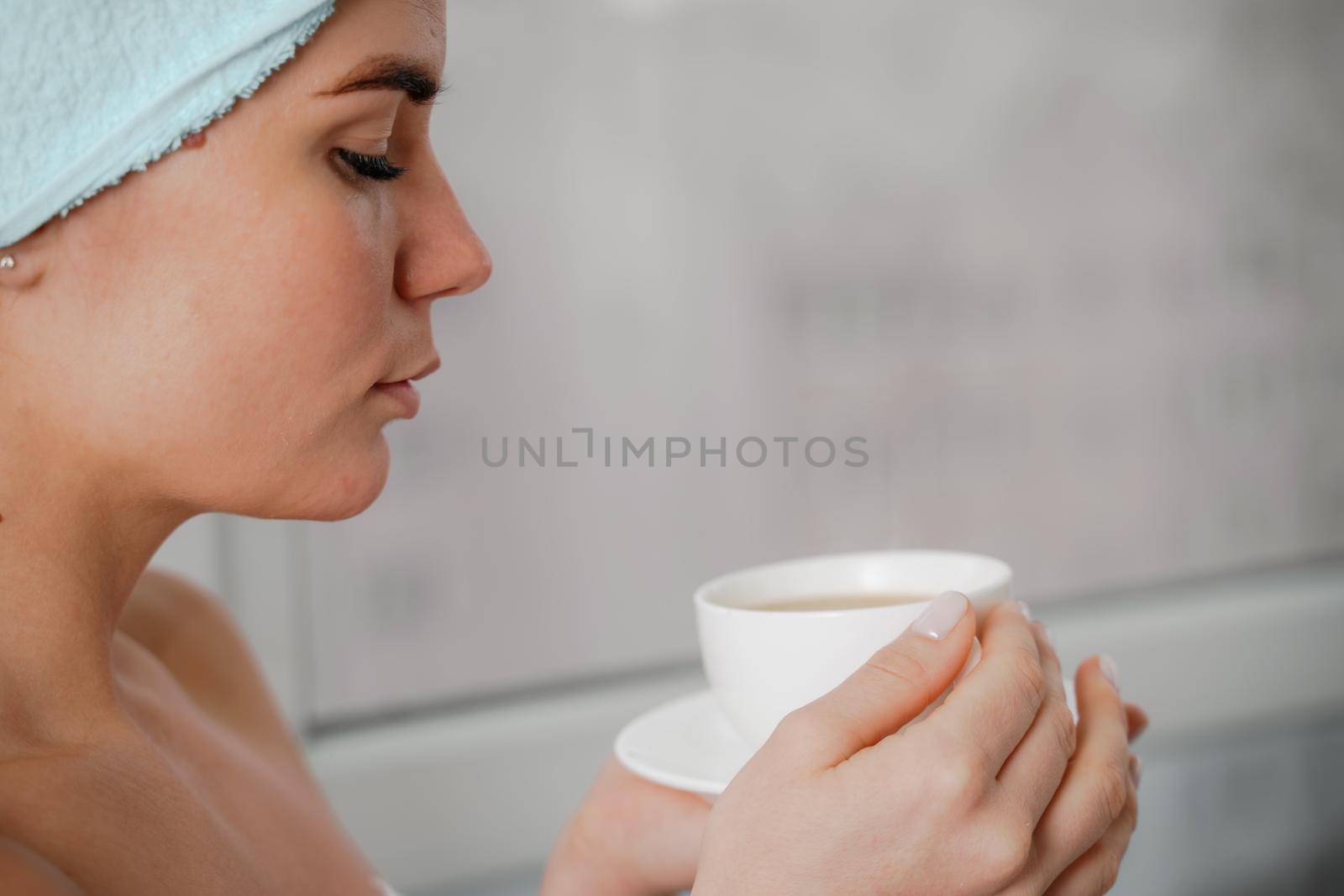 Young serene relaxed woman in spa bath towel drinking hot beverage tea coffee after taking shower bath at home. Beauty treatment, hydration concept