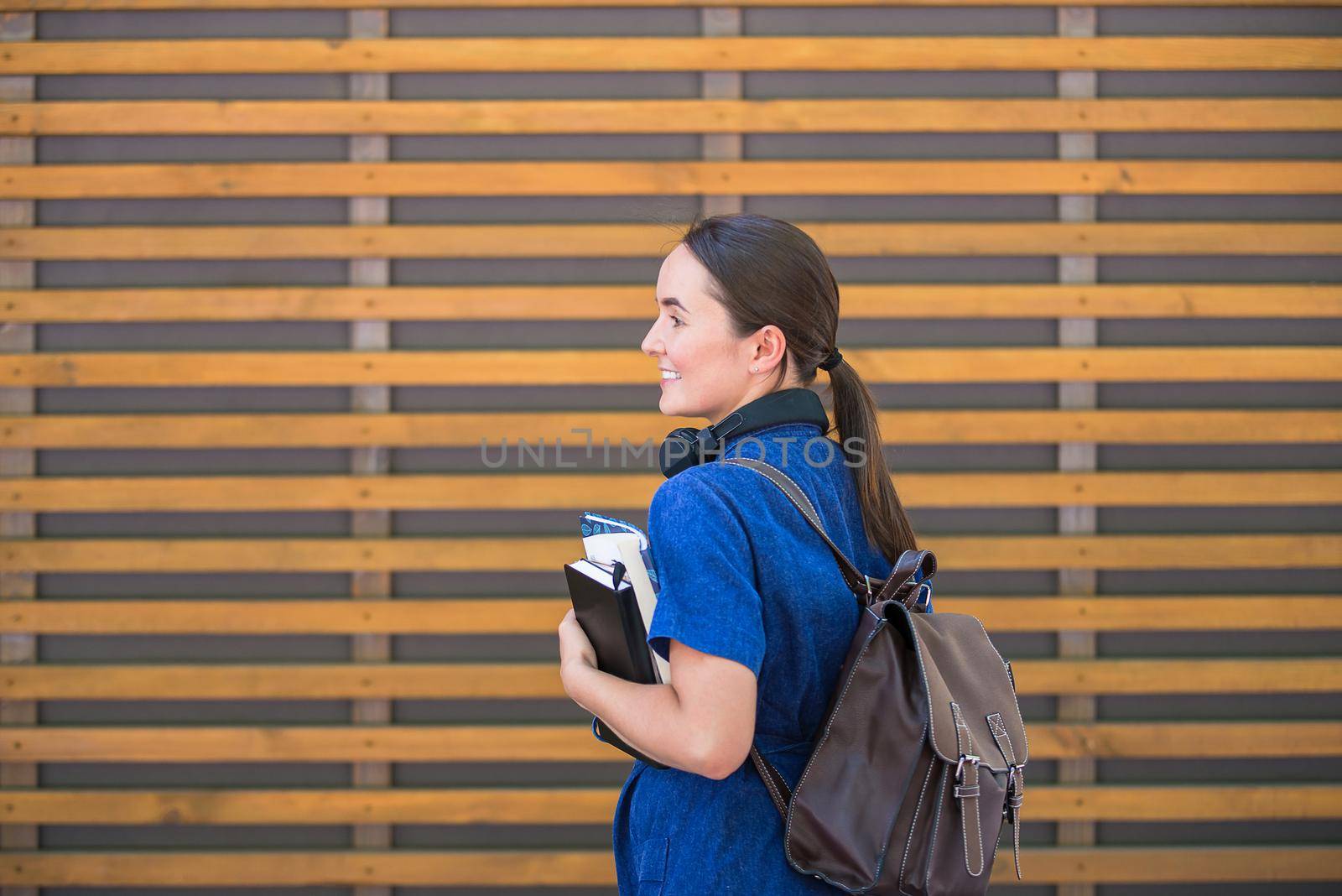 student girl is standing near wooden wall holding books