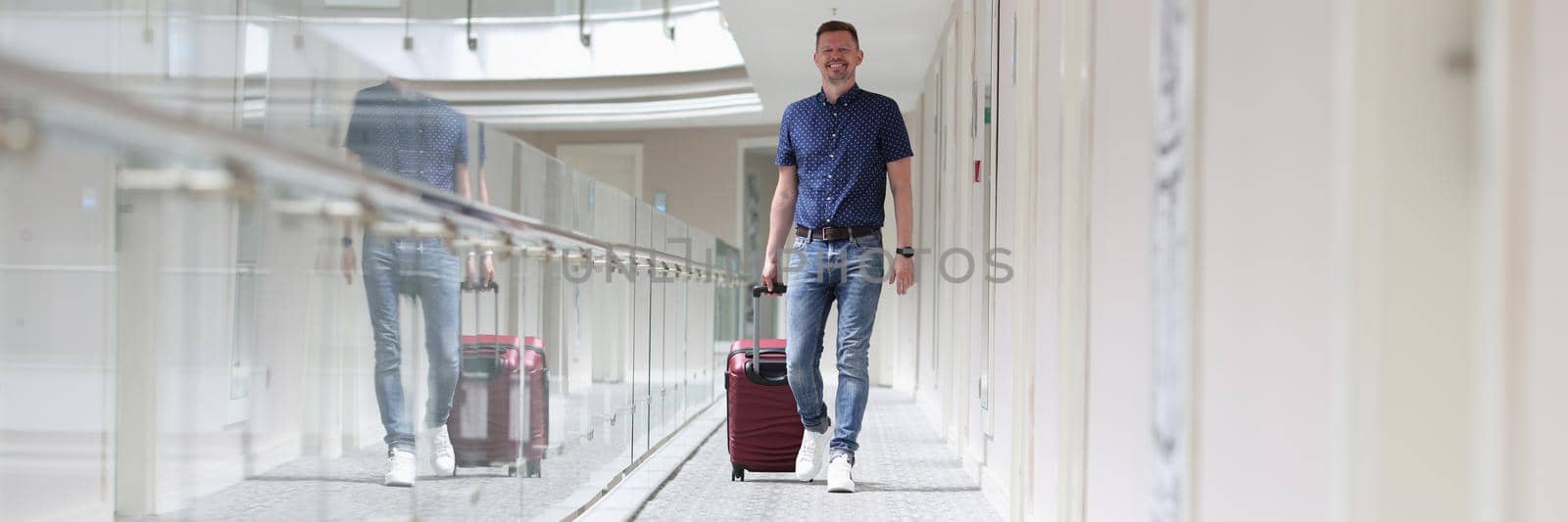 Young man with suitcase walking down hotel corridor. Tourism and recreation abroad concept