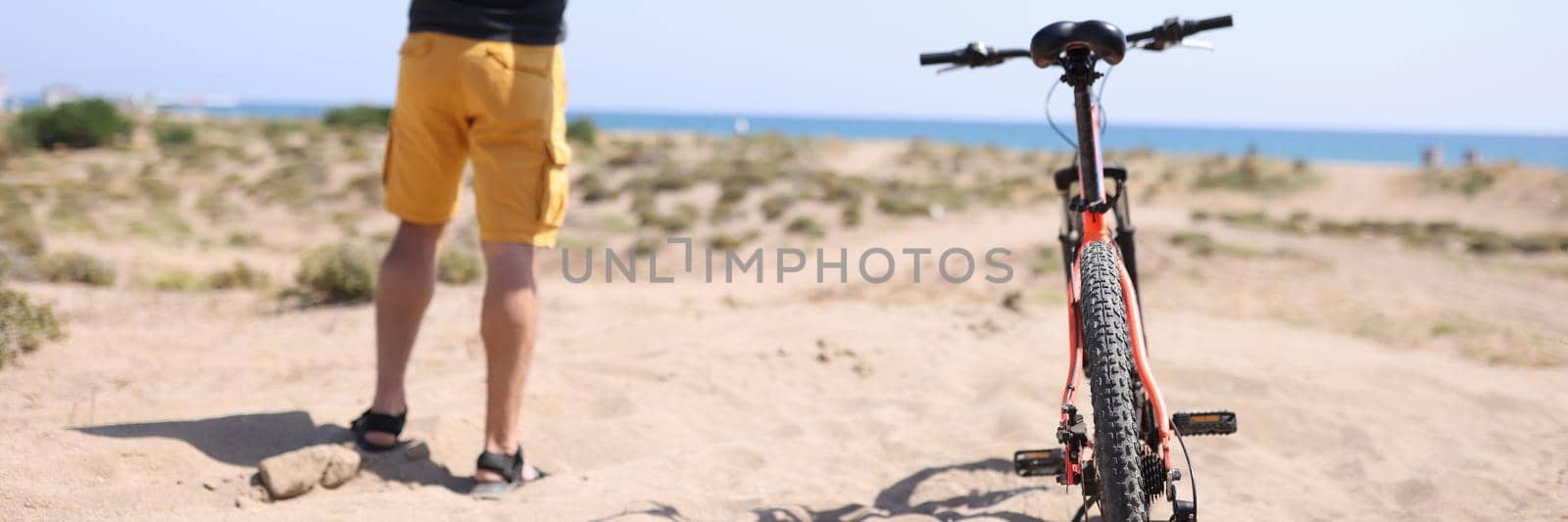 Man standing on beach near bicycle with his arms wide apart back view. Goal achievement concept