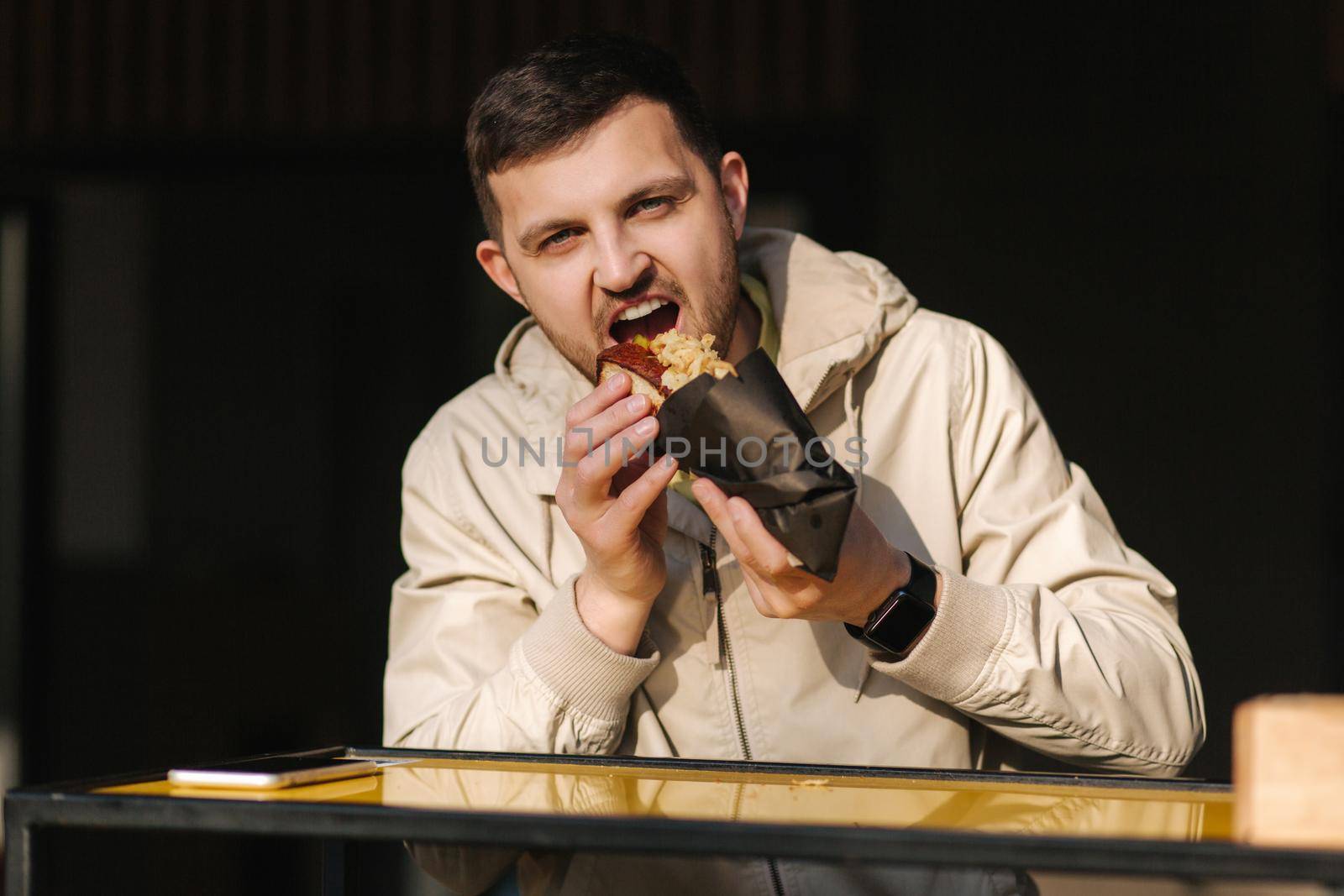 Handsome man having traditional hot dog cuisine during rest break. Caucasian guy enjoying street cuisine outdoor. Male eating unhealthy fast food.