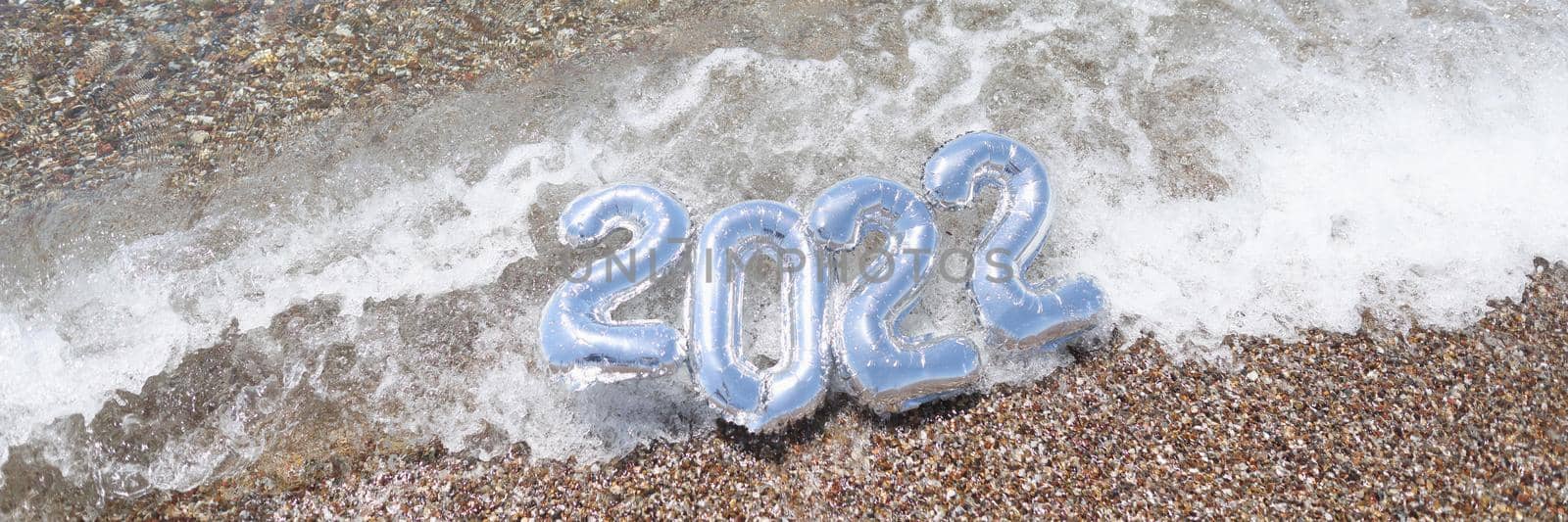 Helium balloons with numbers 2022 lying on sea wave closeup background. Travel in new year concept