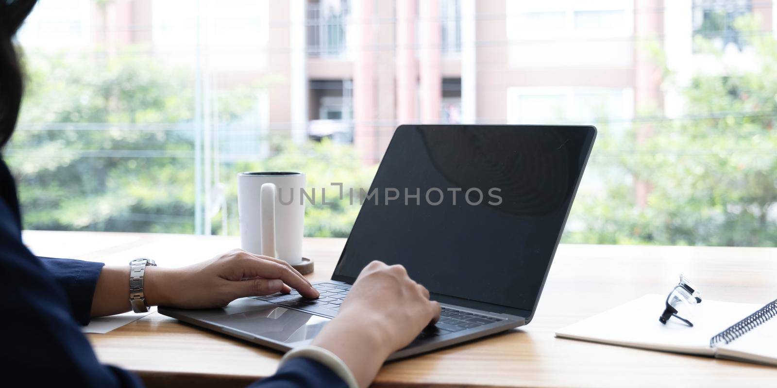 Over shoulder close up view of female hands typing on laptop with mock-up screen on office desk with stationery.