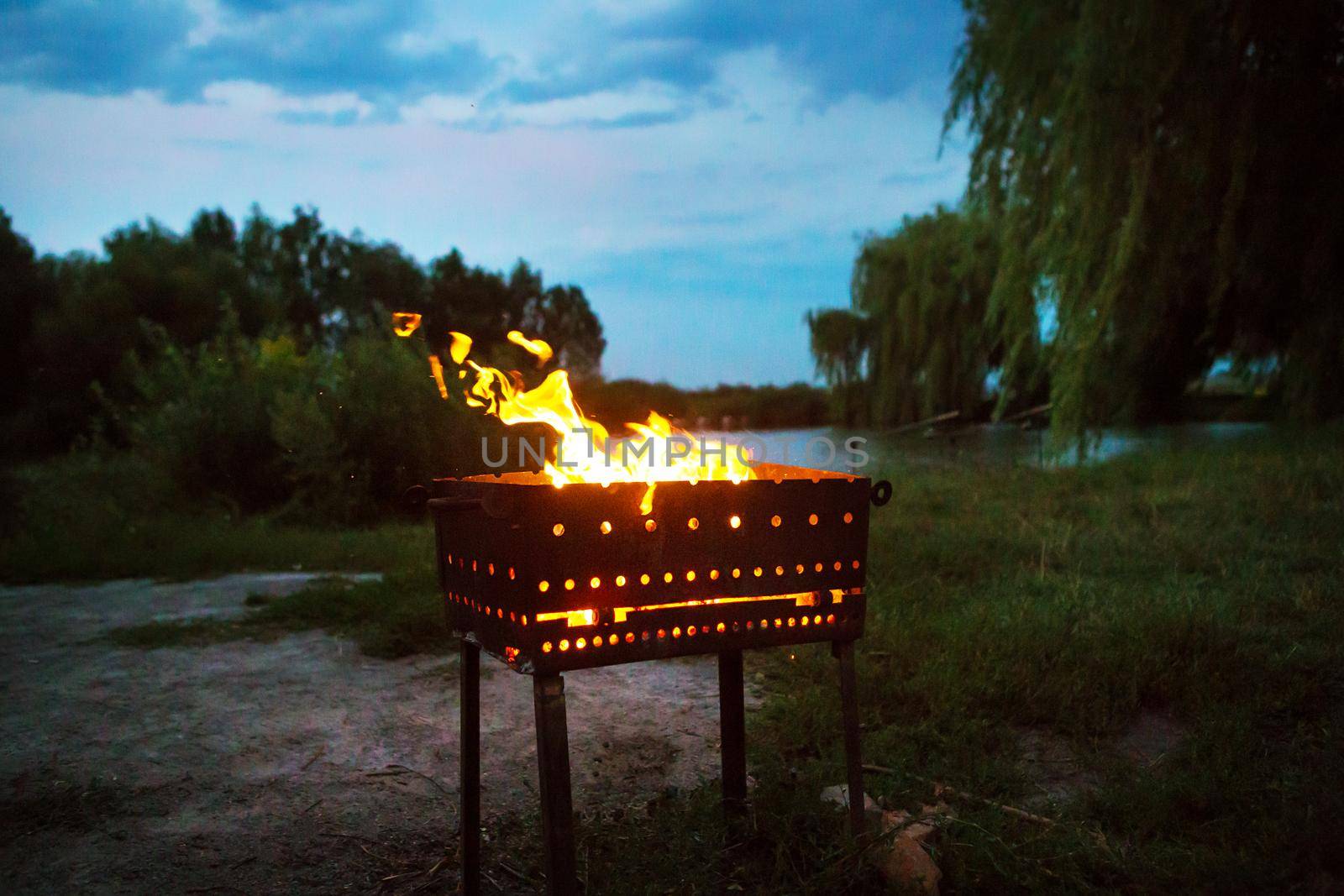 evening landscape - burning firewood in the grill: preparation for the frying of meat, near the lake by sfinks