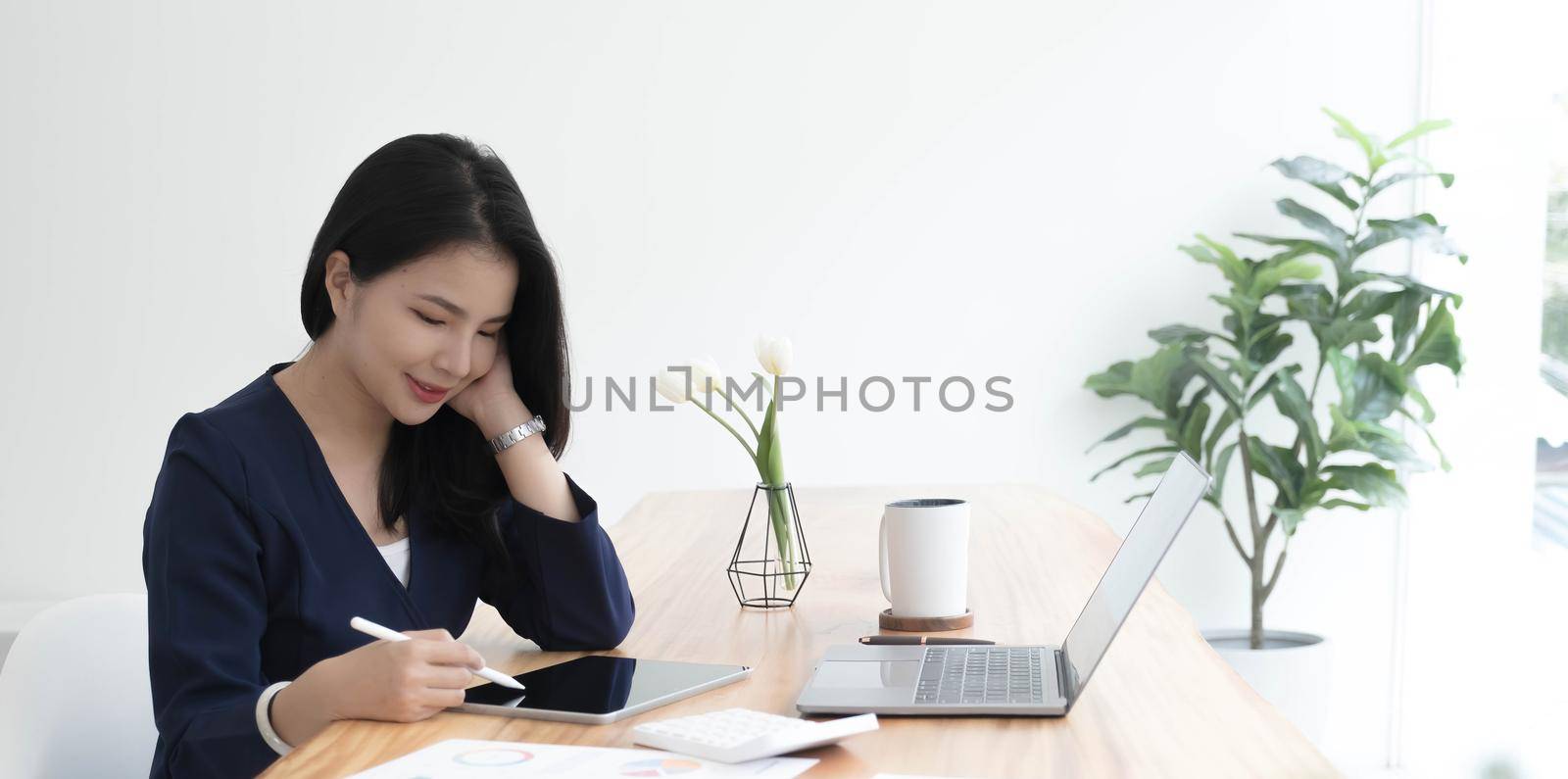 Young asian businesswoman works on tablet with laptop at the office. by wichayada
