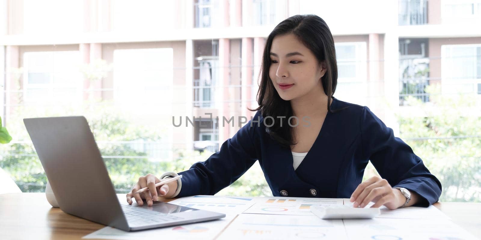 Happy young asian businesswoman sitting on her workplace in the office. Young woman working at laptop in the office. by wichayada