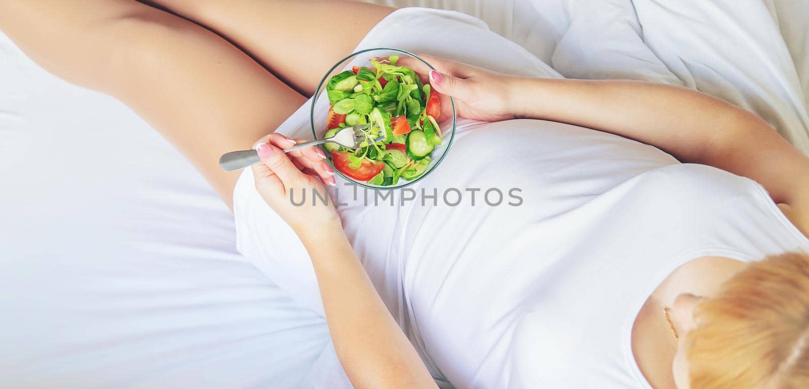 A pregnant woman eats a salad with vegetables. Selective focus. Food.