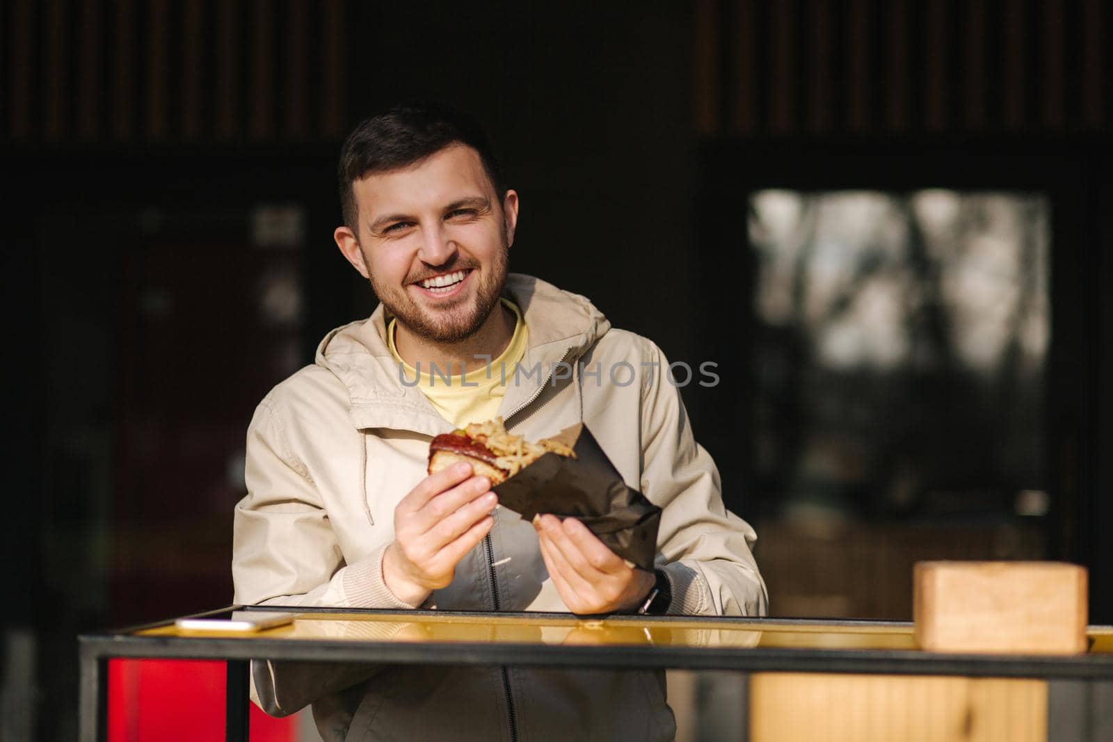 Handsome man having traditional hot dog cuisine during rest break. Caucasian guy enjoying street cuisine outdoor. Male eating unhealthy fast food.