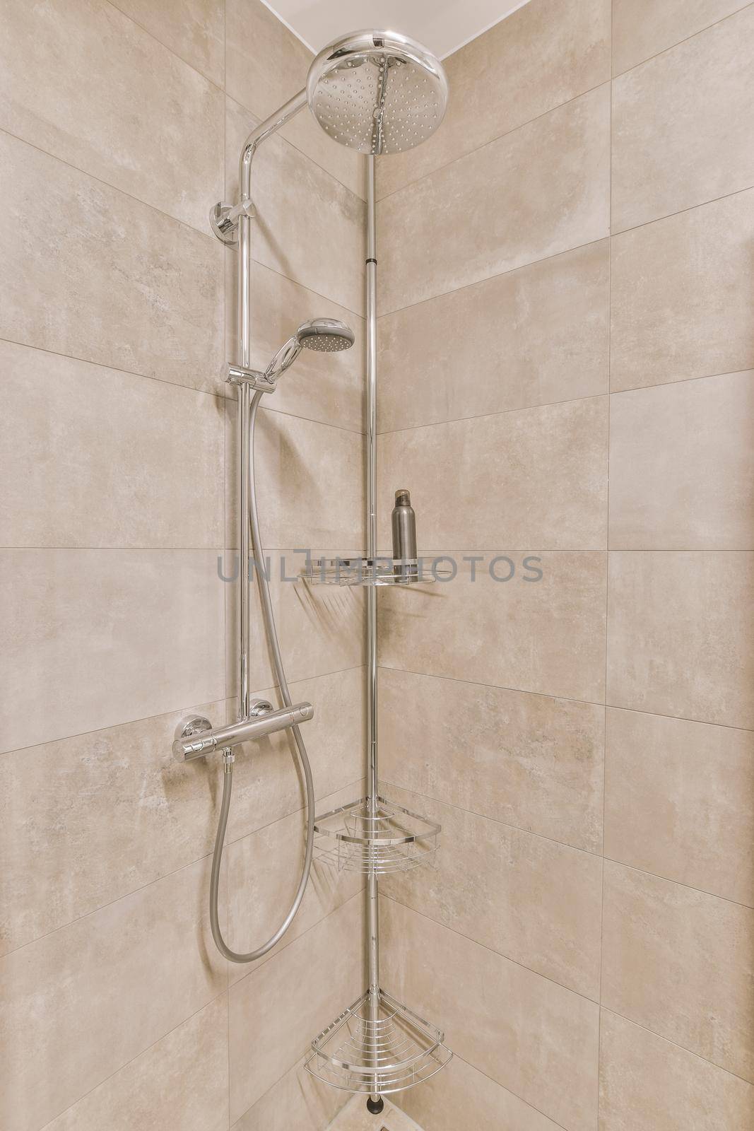 Shower faucets attached to tiled wall near glass partition and ornamental curtail in washroom at home